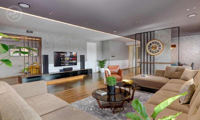 Large living room in Hyderabad with twin beige sofas, glass coffee table, wall-mounted TV and metal-clock room divider