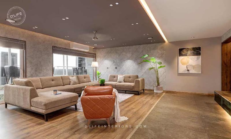 Living room with sectional and corner sofas, tan leather armchair, tall planter and abstract wall art on textured walls, Hyderabad