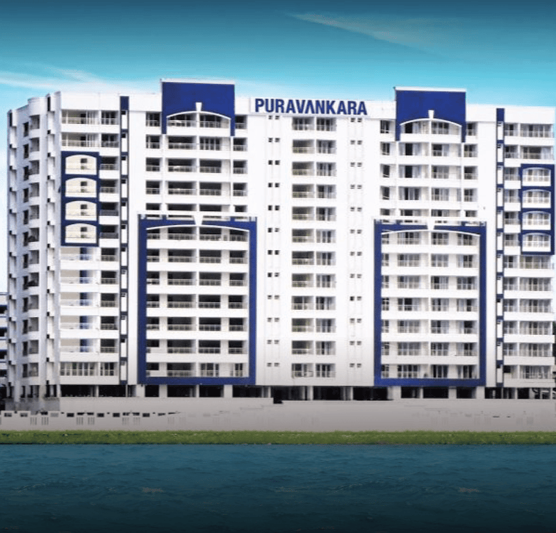 Puravankara apartment tower exterior with white and blue facade and curved balconies beside water, Hyderabad