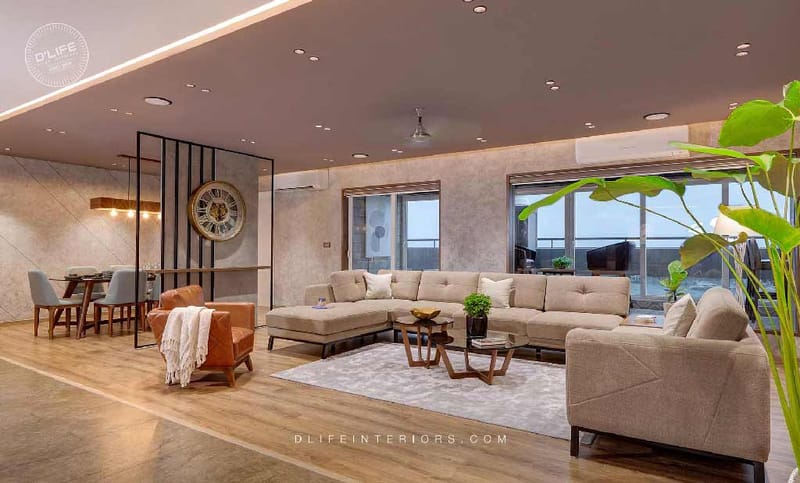 Spacious living and dining space with L-shaped beige sofa, tan leather chair, oversized wall clock and balcony views, Hyderabad