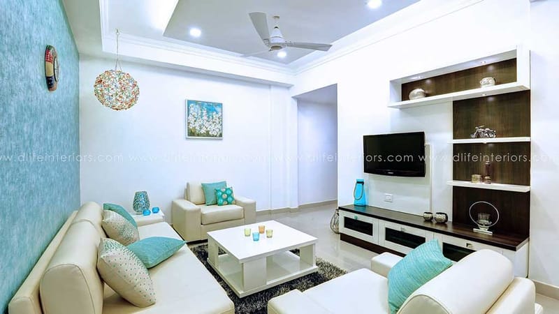 Living room with teal accent wall, white sectional sofa, turquoise cushions and dark TV unit in Hyderabad apartment