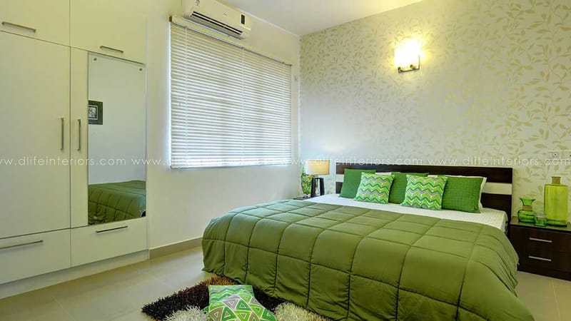 Green-themed bedroom in Hyderabad with leaf-patterned wallpaper, olive bedspread, mirrored wardrobe and wall sconce
