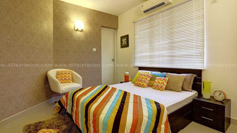 Bedroom with paisley wallpaper, multicoloured striped bedspread, white tub chair and wall sconce, Hyderabad