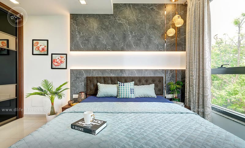 Master bedroom with grey marble headboard wall, navy bedspread and cluster pendant lights beside a leafy window, Hyderabad