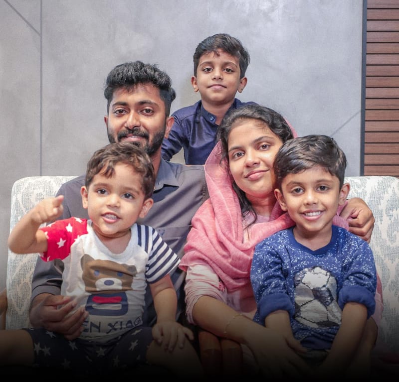 Family of five seated together on a patterned sofa against a grey marble and wood-slat wall, Hyderabad home