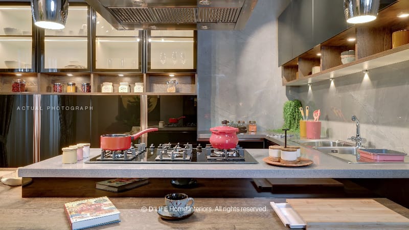 Kitchen detail with grey stone island, dual gas hobs, glass-front upper cabinets and red cookware against a dark backsplash, Hyderabad