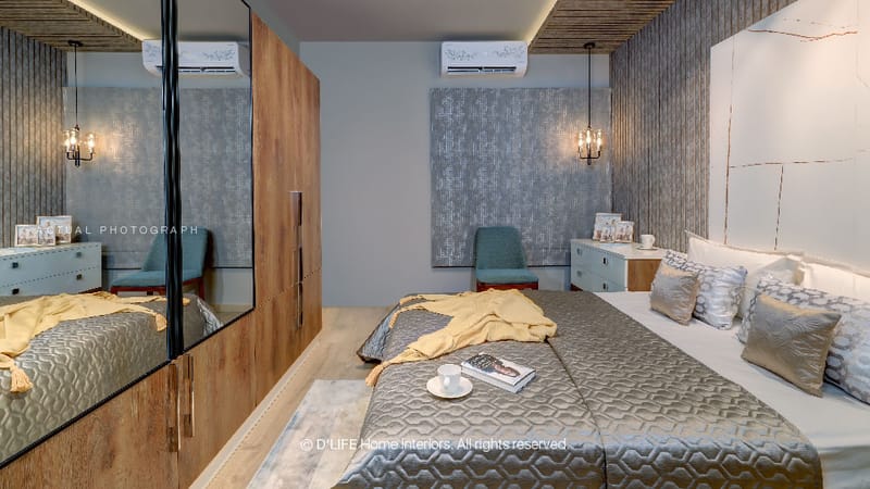 Bedroom with patterned grey wallpaper, wood-toned sliding wardrobe with mirror panel, teal accent chair and quilted bedspread, Hyderabad
