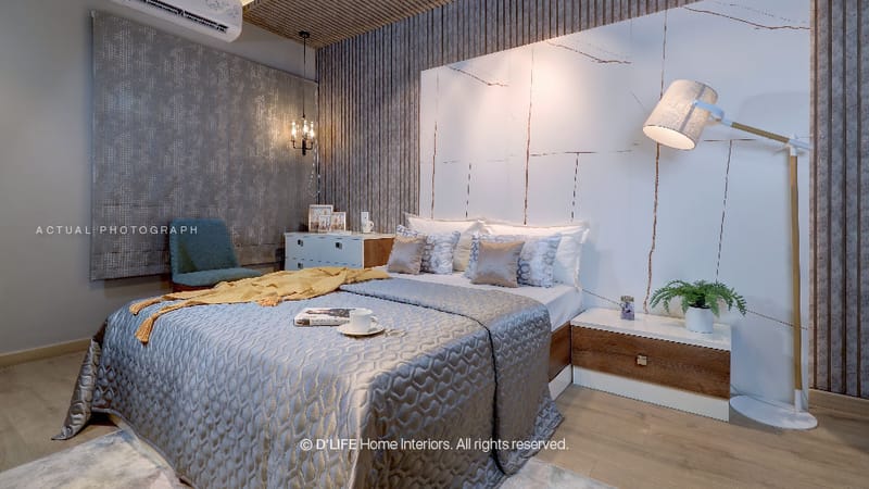 Studio apartment bedroom with grey textured accent wall, quilted silver bedding, mustard throw and arc floor lamp, Hyderabad