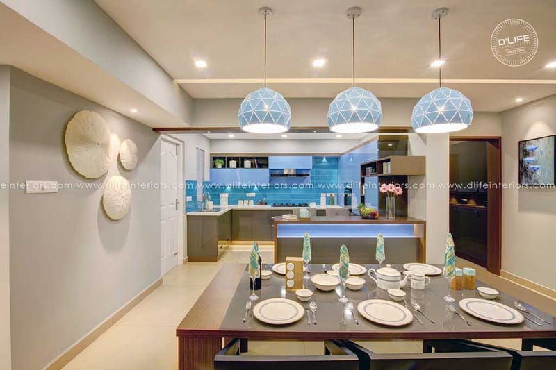 Dining space set for a meal under blue geometric pendant lamps with sculptural disc wall art and blue island kitchen, Hyderabad