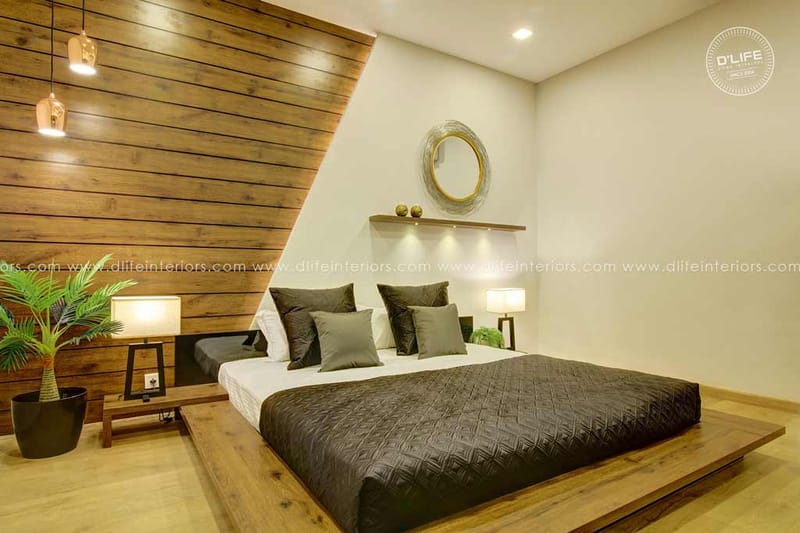 Bedroom with low platform bed, dark quilt and angled wood-clad headboard wall with round mirror and pendant lights, Hyderabad