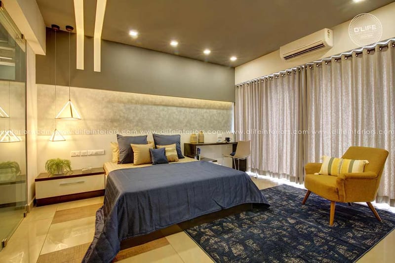 Contemporary bedroom with cushioned grey headboard wall, blue-grey bedding and mustard accent chair, Hyderabad