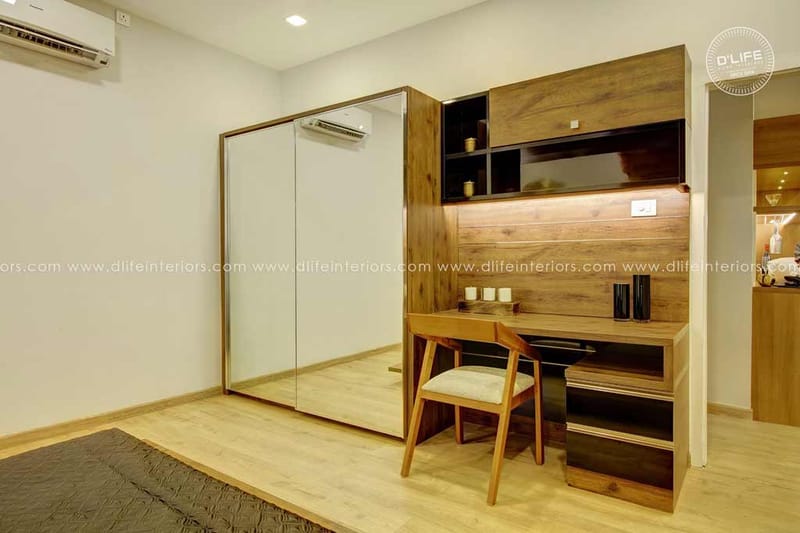 Bedroom with mirrored sliding wardrobe and walnut study desk featuring backlit shelving and a cane chair, Hyderabad