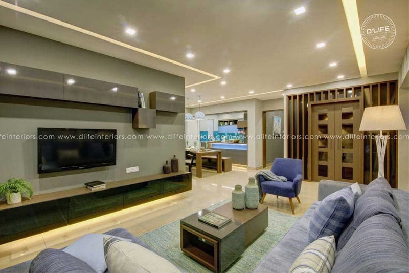 Spacious living room with grey TV unit wall, blue accent armchair, slatted glazed doors and view to kitchen, Hyderabad