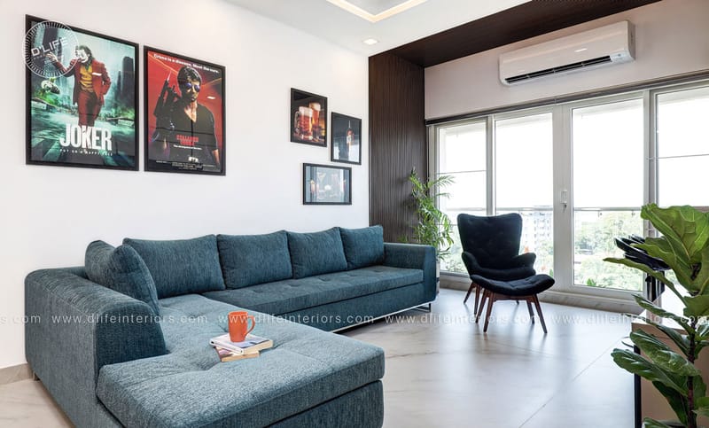 Living room with teal L-shaped sectional, framed Joker movie posters and a navy accent chair, Hyderabad