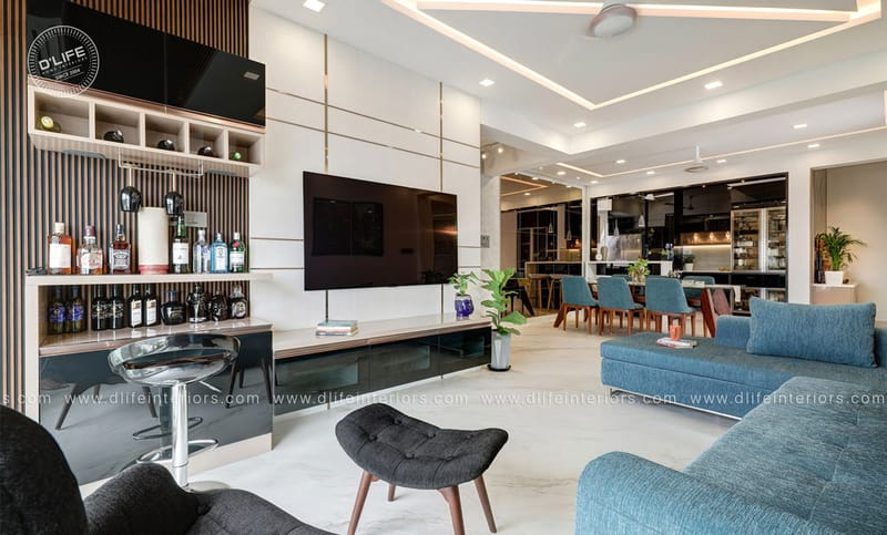 Open living room with wall-mounted TV unit, fluted home bar with wine display and teal sofas opening to a dining area, Hyderabad