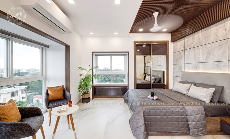 Master bedroom with wooden-slat ceiling, marble accent wall, grey upholstered bed and a window sitting nook, Hyderabad