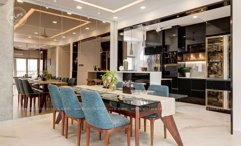 Open-plan dining and kitchen with glossy black cabinetry, glass-top wood table and blue upholstered chairs, Hyderabad