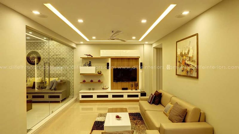 Living room with cove-lit false ceiling, wood-and-white TV unit, beige sofa, glass partition and abstract art, Hyderabad
