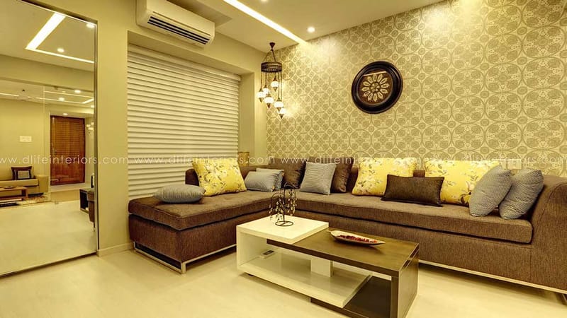 Living room featuring grey-brown corner sofa, patterned wallpaper, decorative wall clock and white coffee table, Hyderabad