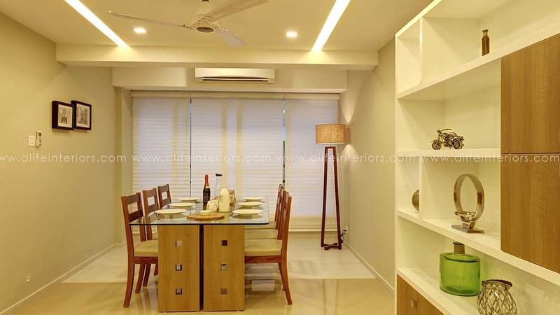 Dining area with glass-top wooden table, four chairs, open display shelving and a slim floor lamp, Hyderabad