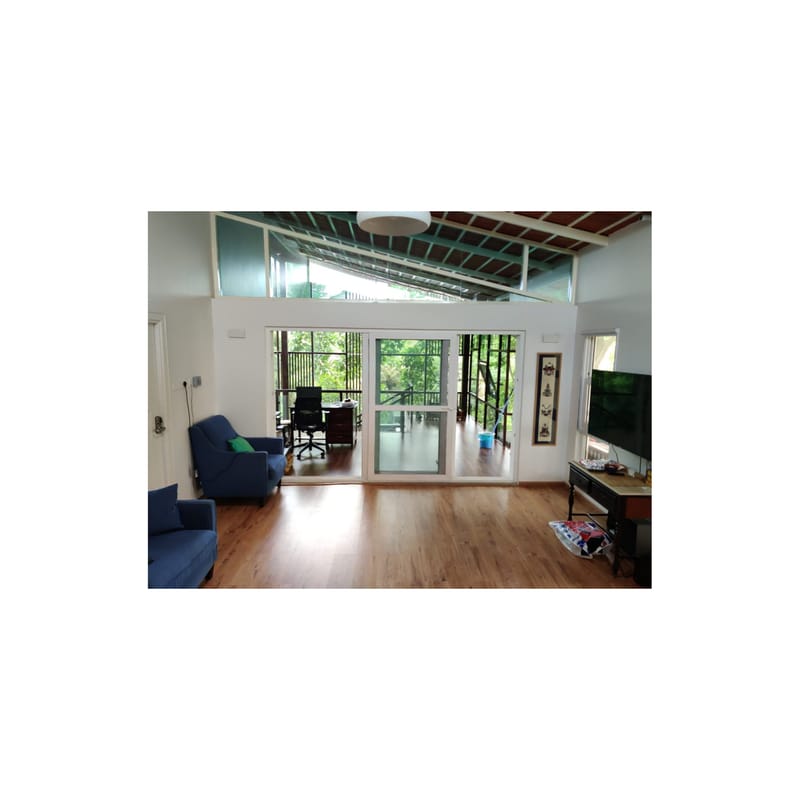 Double-height living room with blue sofas, warm wood flooring and sliding glass doors opening to greenery, Hyderabad