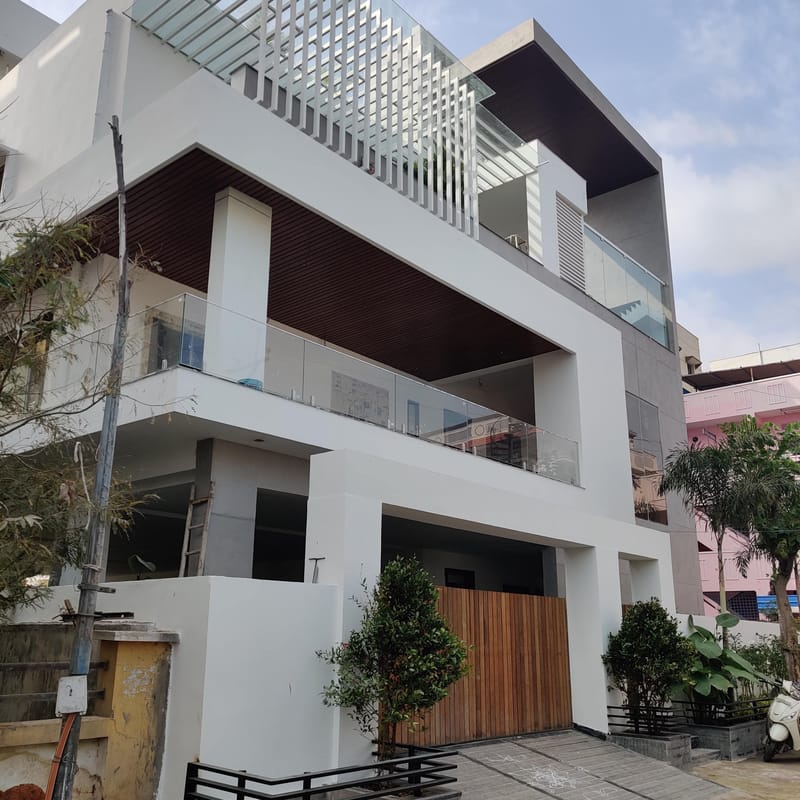 Modern three-storey home exterior with wood-slat balcony soffits, glass-railed terraces and a rooftop pergola, Hyderabad