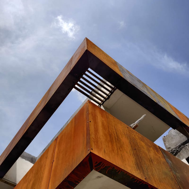 Upward detail of a weathered Corten-steel roof overhang and slatted brise-soleil against the sky, Hyderabad villa