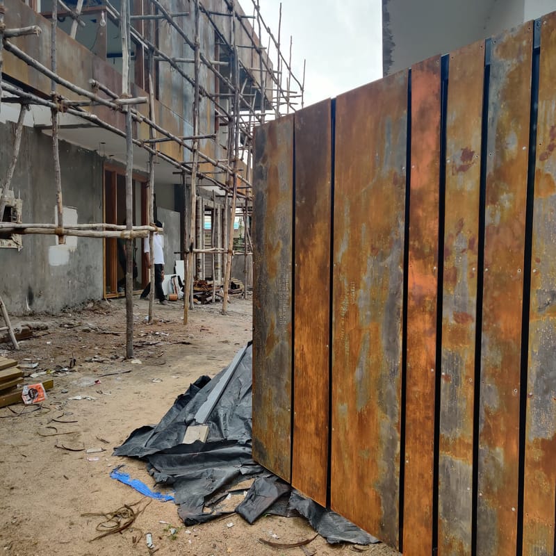 On-site Corten-steel cladding panels with weathered patina beside scaffolding during villa construction, Hyderabad