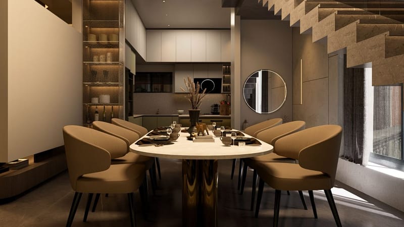 Oval dining table with tan chairs, gold pedestal base and an open kitchen behind in moody lighting, Hyderabad full home