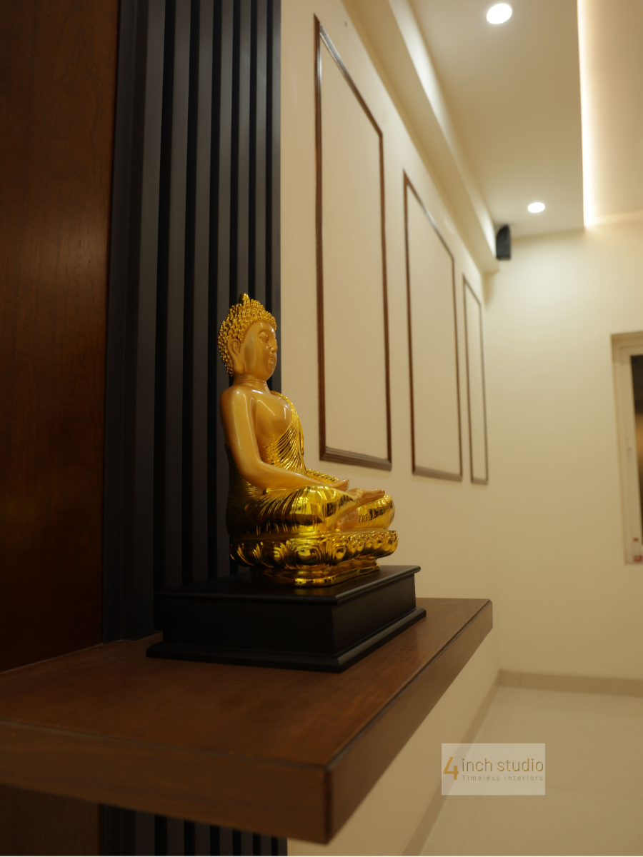 Golden Buddha statue on a wood shelf against a fluted black panel with framed wall art in a Hyderabad home