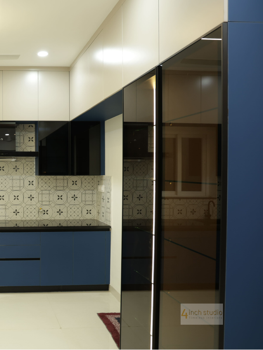 Modular kitchen edge with navy cabinets beside a glossy bronze glass sliding partition, Hyderabad apartment
