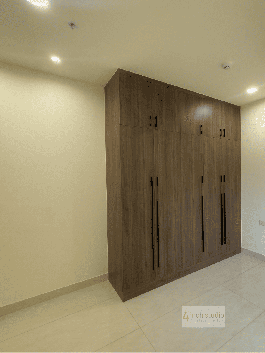 L-corner walnut wardrobe with loft storage and recessed lighting against a pale bedroom wall, Hyderabad