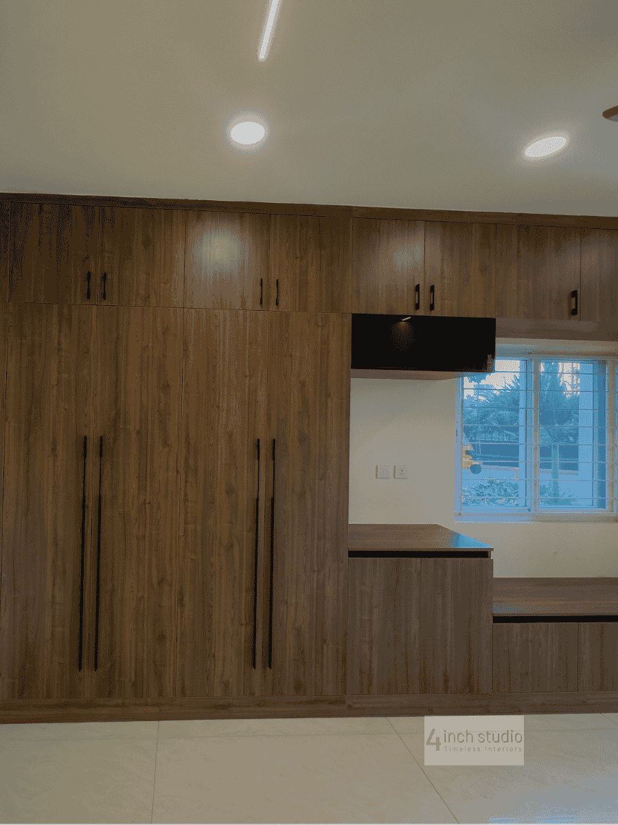 Bedroom wall of dark walnut wardrobes with TV niche and a window-side study ledge, Hyderabad apartment