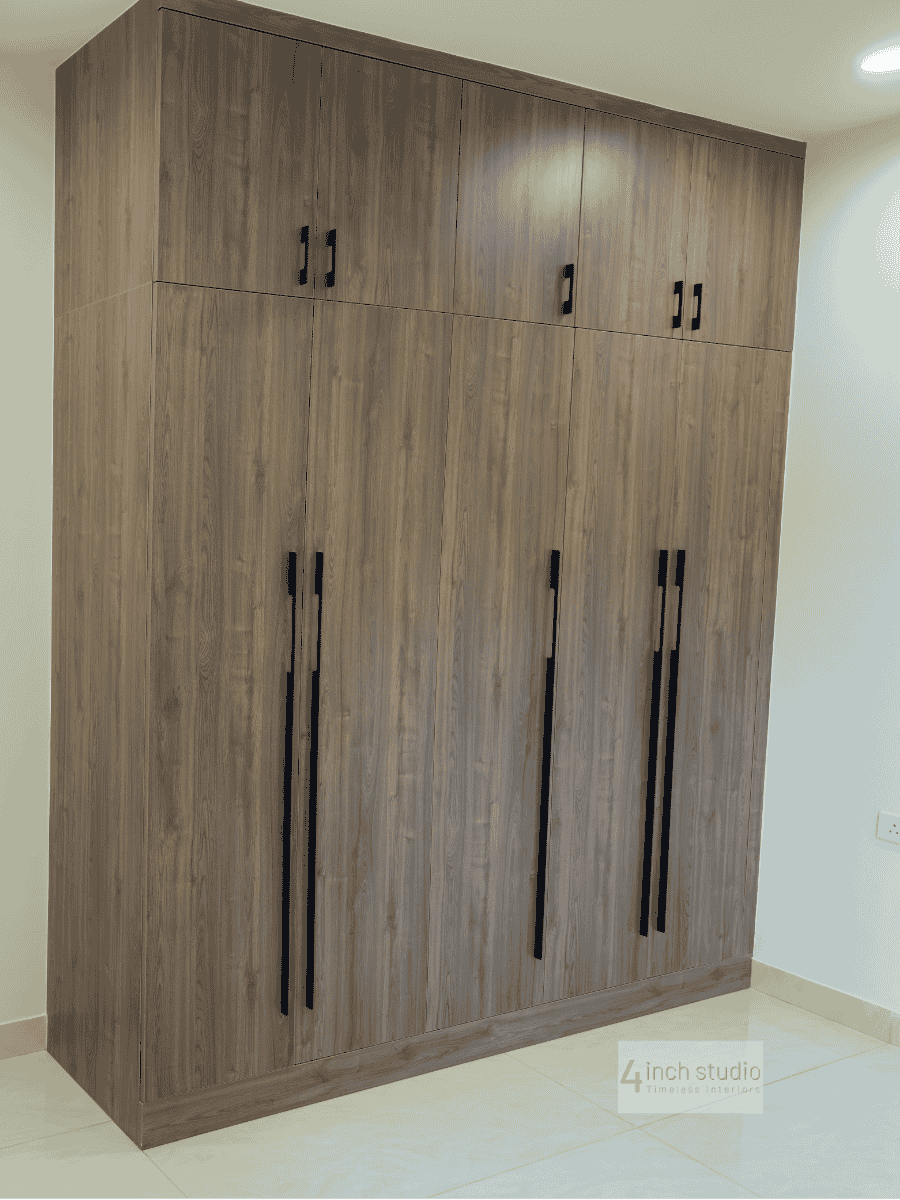 Tall grey-wood wardrobe with overhead loft cabinets and vertical black pulls in a bedroom corner, Hyderabad