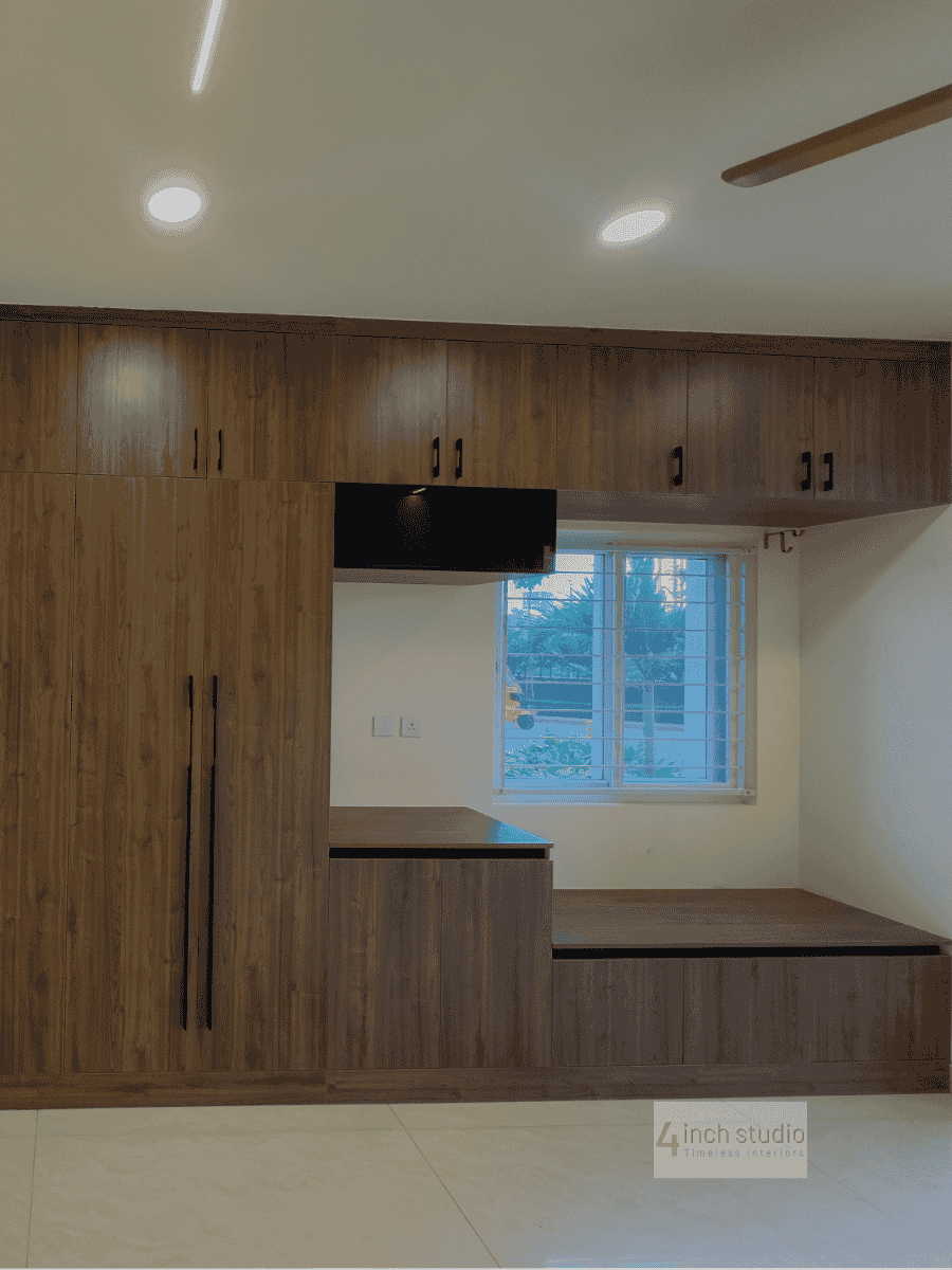 Floor-to-ceiling walnut wardrobes wrapping a window seat and TV recess in a bright bedroom, Hyderabad