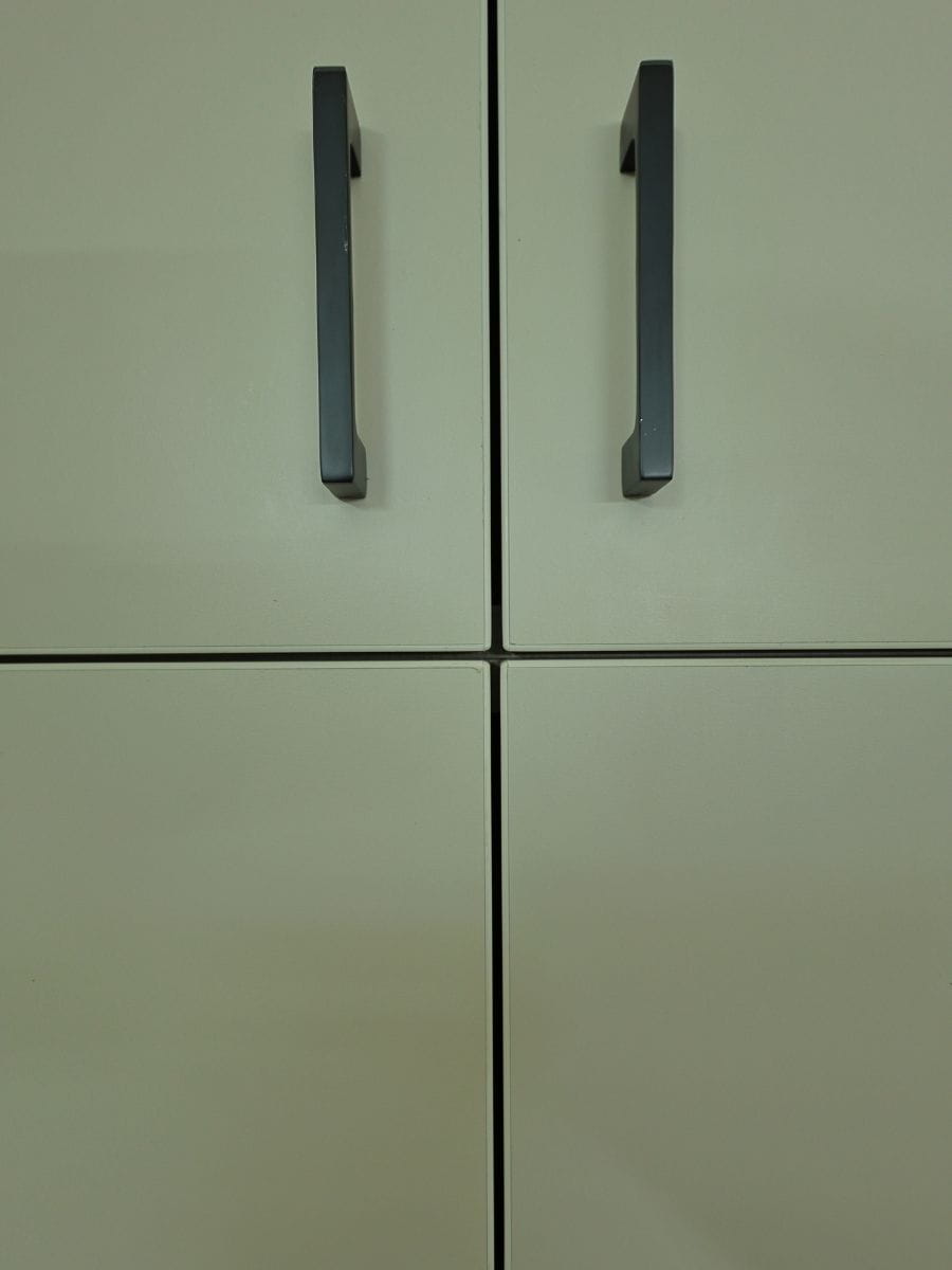 Close-up of off-white cabinet shutters with slim black bar handles and crisp grooved joints, Hyderabad