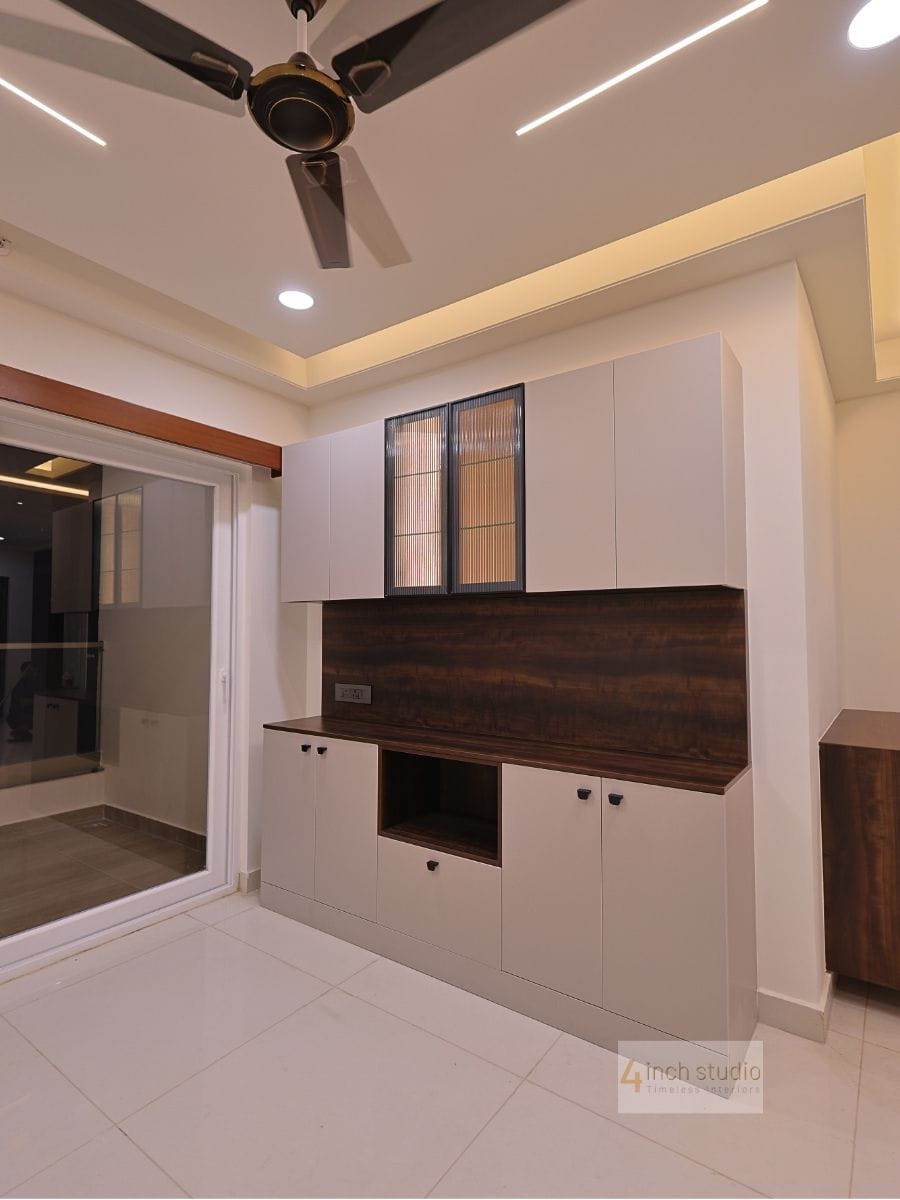 Living-dining storage unit with white cabinets, fluted-glass doors and dark wood backsplash beside a sliding glass door, Hyderabad
