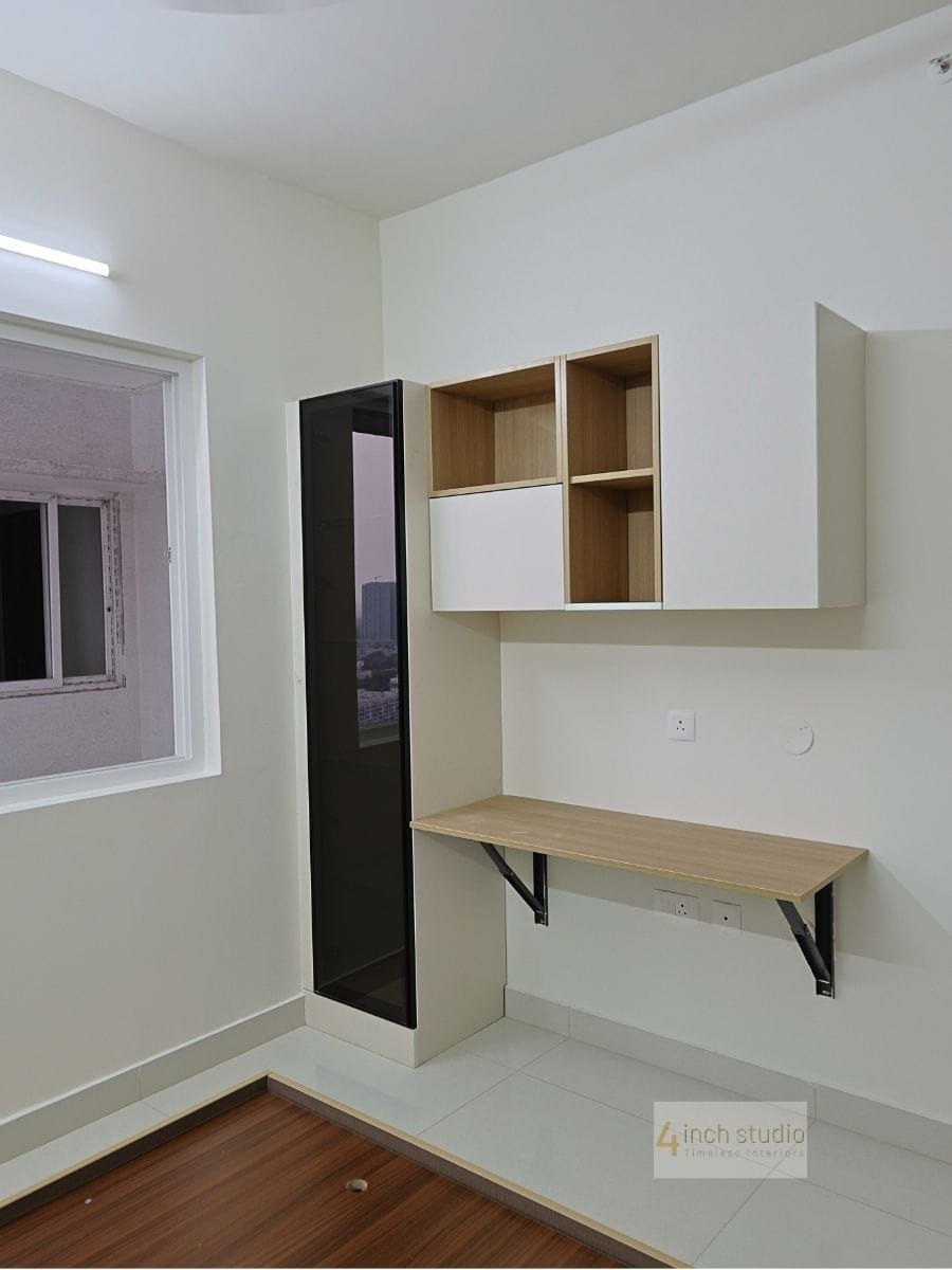 Bedroom study corner with floating wooden desk, open shelf unit and slim tinted-glass tall cabinet by the window, Hyderabad