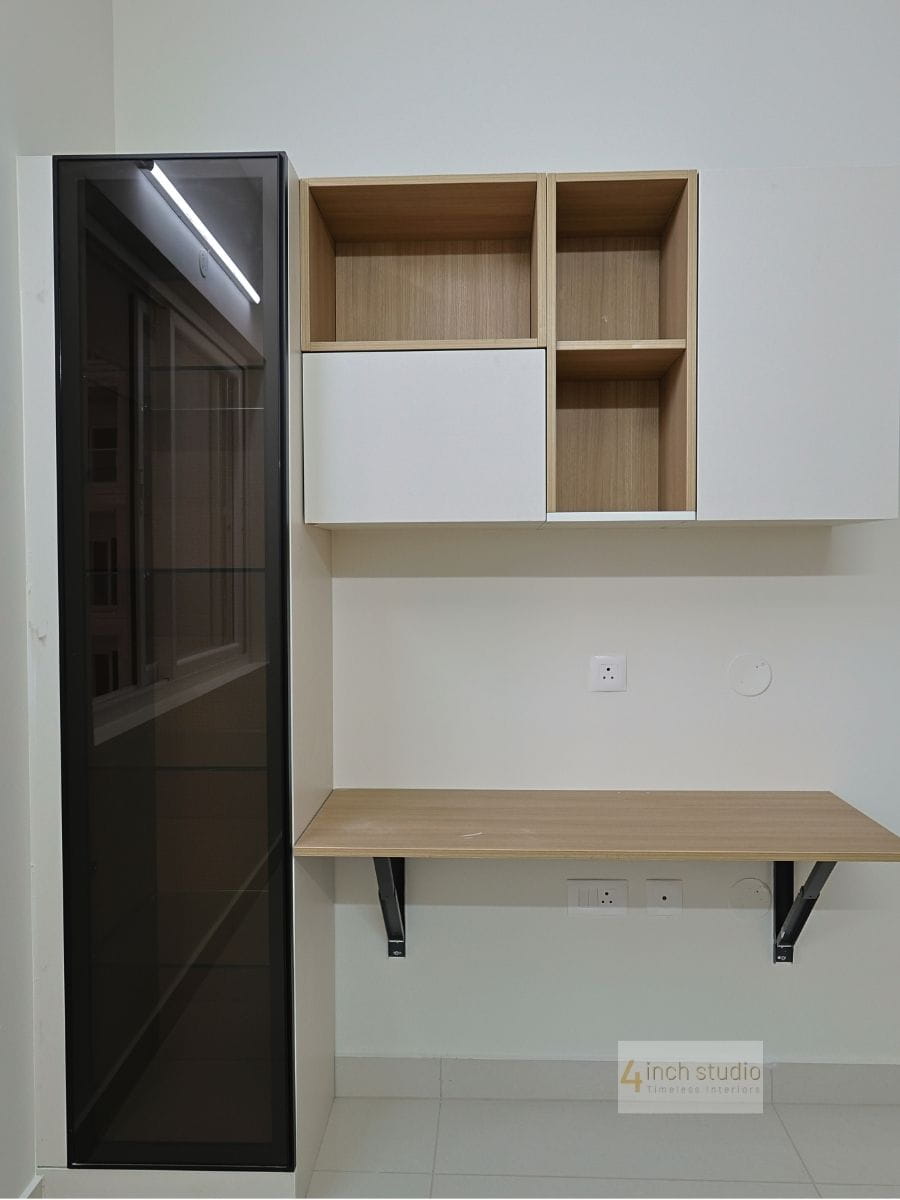 Study nook with wall-mounted wood desk, open shelves with sliding box and tall tinted-glass cabinet, Hyderabad apartment