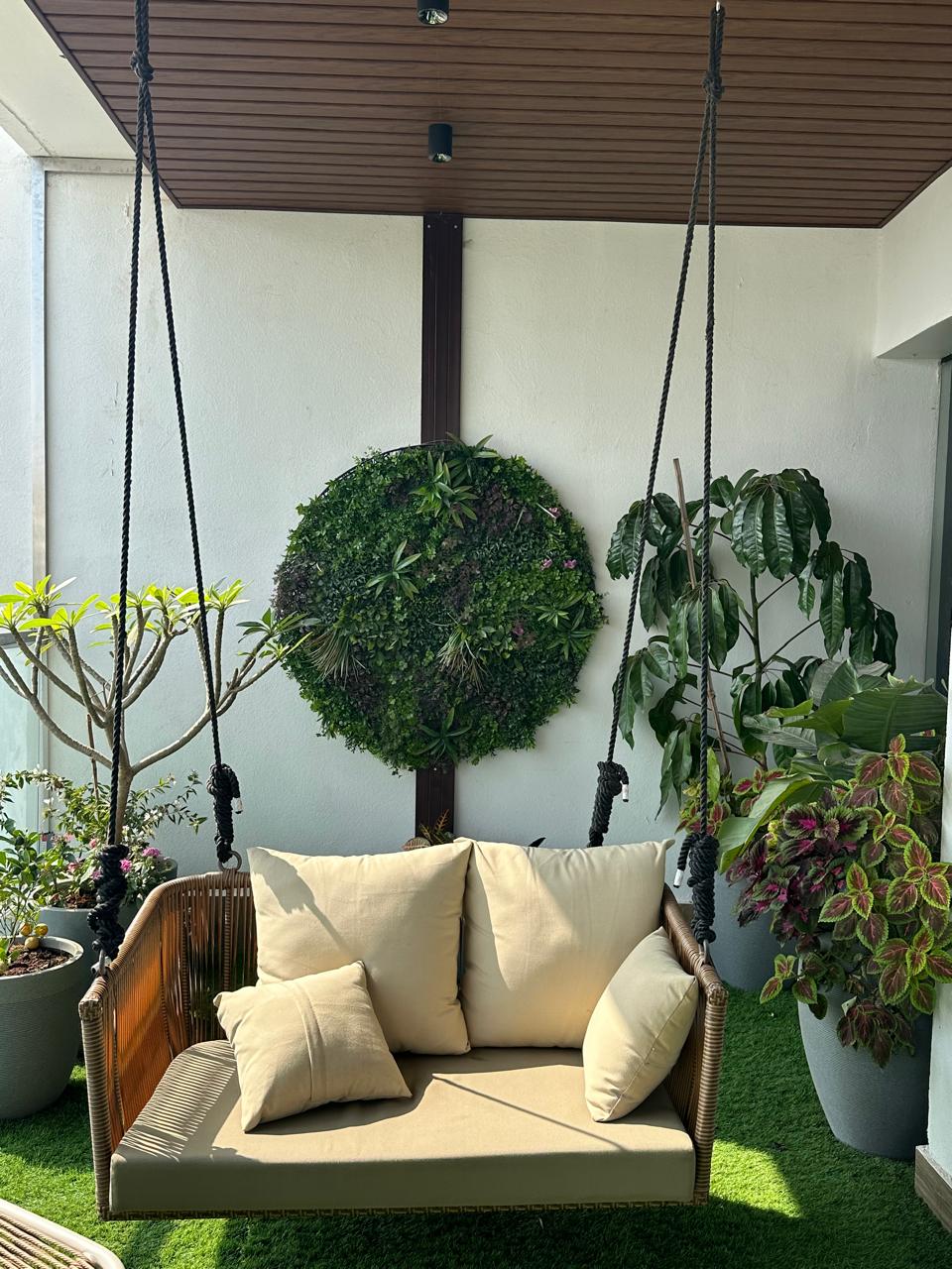 Balcony swing seat with cream cushions beside a round vertical garden and potted plants, Hyderabad