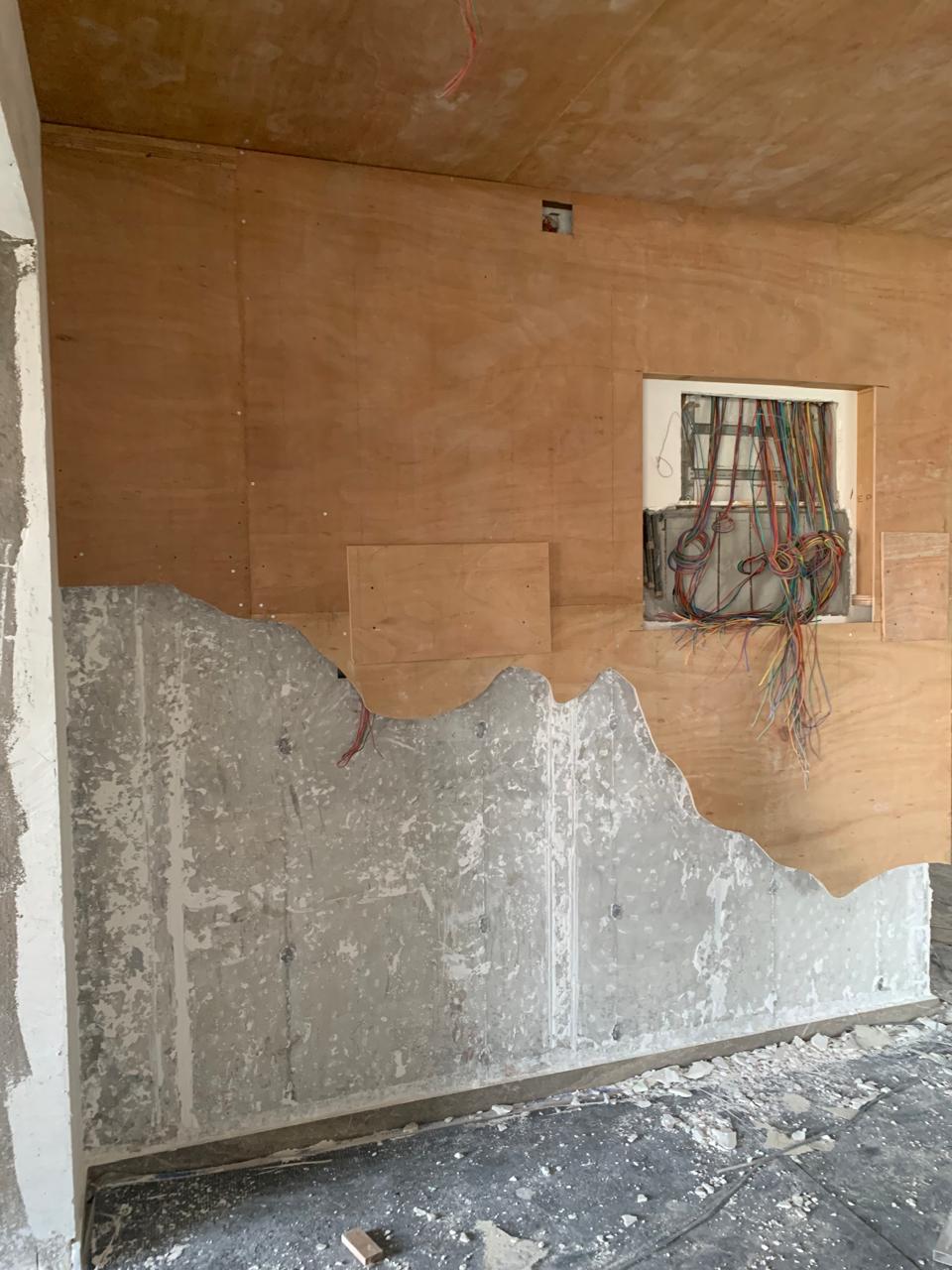 Living room mid-renovation in Hyderabad with plywood-clad wall, exposed electrical wiring and a half-demolished concrete wall