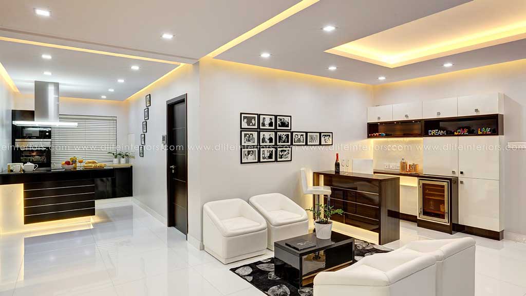 Open-plan living and kitchen with glossy white units, black island, photo gallery wall and white tub chairs, Hyderabad