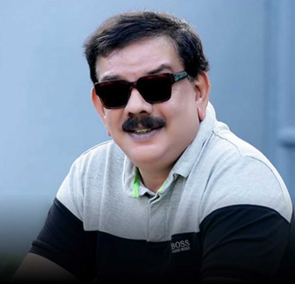 Headshot of a man in sunglasses and a grey-and-black polo shirt against a plain backdrop